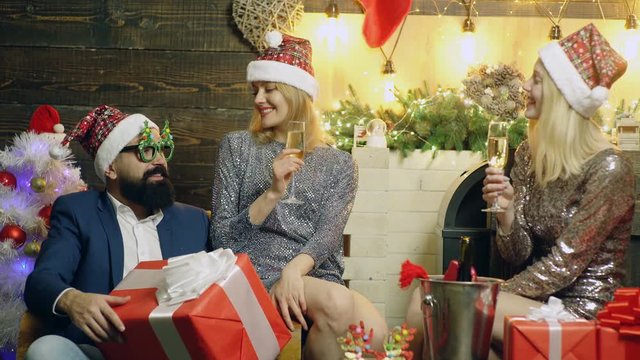 Bearded man and two prety girls drink champagne near the New Year's background. Young people celebrate Christmas. New Year's mood. Christmas presents near the Christmas tree.