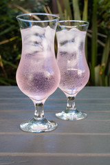 two glasses of pink craft gin and tonic on a wooden table in a garden setting