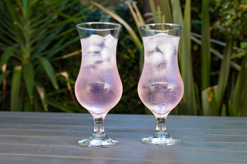 two glasses of pink craft gin and tonic on a wooden table in a garden setting