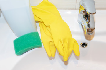 Yellow rubber gloves, sponge and washing detergent bottle on bathroom sink