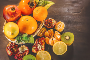 citrus fruits in a wooden basket. orange, pomegranate, mandarin, persimmon, kiwi. on a dark wooden board.