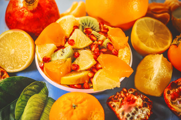 Fototapeta na wymiar cut scitrus fruits. orange, pomegranate, mandarin, persimmon, kiwi. on a blue wooden board.