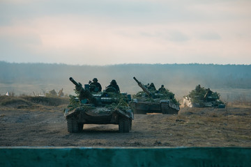 Tanks in row masked at pine tree branches in polygon © yarohork