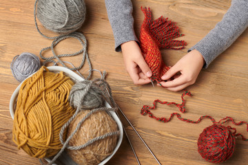 Child girl is learning to knit. Colorful wool yarns are on the wooden table. Hand closeup.