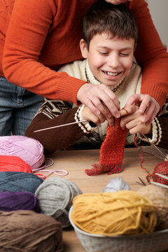 Mother is learning her child boy to knit. Colorful wool yarns are on the wooden table.