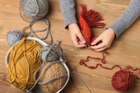 Child girl is learning to knit. Colorful wool yarns are on the wooden table. Hand closeup.
