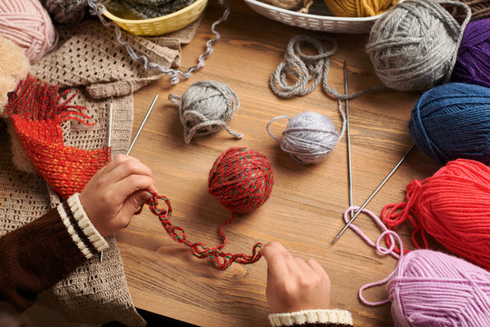 Child boy is learning to knit. Colorful wool yarns are on the wooden table. They are placed as smiling face. Hand closeup.