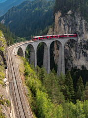 Roter Zug auf der berühmten Brücke des Landwasserviadukts. Der Abschnitt der Rhätischen Bahn aus dem Albula/Bernina-Gebiet (der Teil von Thusis nach Tirano, einschließlich St. Moritz), Schweiz, Europa. August 2018