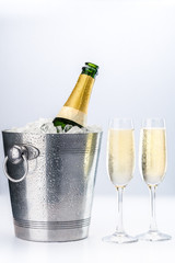 Champagne bottle on ice cubes in a bucket with two glasses of champagne.