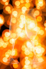 Two champagne glasses with yellow and orange lights in the background.