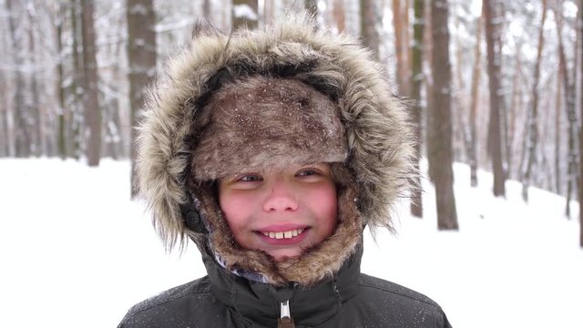 Closeup portrait of young cheerful kid with scrapped nose making funny faces outside in winter snowy landscape  background. Real time 4k video footage.