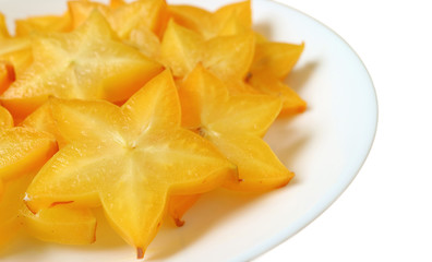 Vibrant orange yellow fresh ripe Star Fruit sliced in pieces served on white plate isolated on white background 