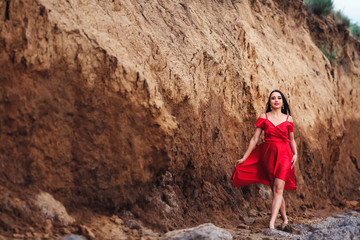 beautiful woman in red dress posing on clay cliff background.