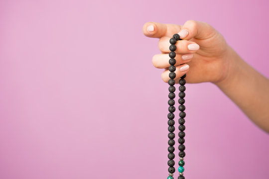 Woman, lit hand close up, counts Malas, strands of gemstones beads used for keeping count during mantra meditations on pink background
