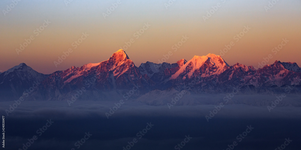 Wall mural Mountain Range Sunrise, mountains glowing in the sunshine at dawn. Snow covered mountain peaks in the distance, panoramic view. Purple, Orange atmosphere. Sichuan Province China. Rugged wilderness