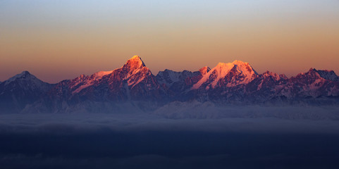 Mountain Range Sunrise, mountains glowing in the sunshine at dawn. Snow covered mountain peaks in the distance, panoramic view. Purple, Orange atmosphere. Sichuan Province China. Rugged wilderness