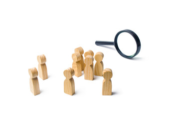 A crowd of wooden human figure stands near a magnifying glass on a white background. The concept of...