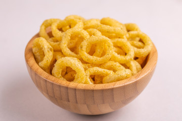 Puff corn rings in wooden bowl on light background
