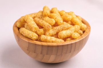 Crispy corn sticks in wooden bowl on light background