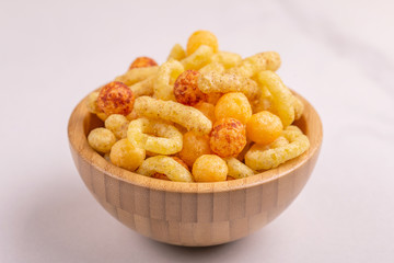 Assorted puff corn snacks in wooden bowl on light background