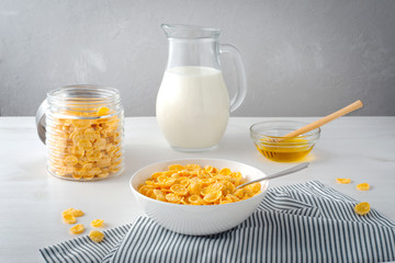 Breakfast with bowl of cornflakes, honey and milk jug on light table. Morning healthy food - 240532033