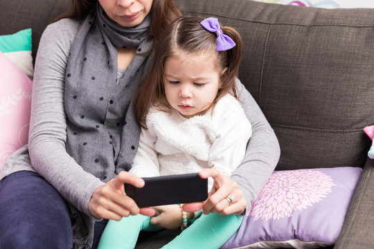 Mother And Daughter Using Mobile Phone On Sofa