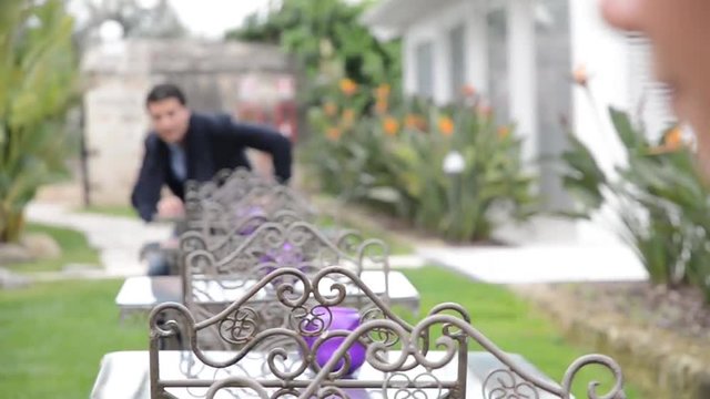 Giovane uomo si siede ad un tavolino in un giardino, osservato da una donna interessata