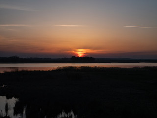 evening rural sunset over small river and forest. low key image. sun is almost disappeared under horizon line