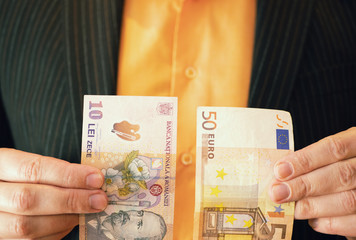businessman in suit holding Romanian lei banknote money in one hand and 50 fifty Euros in other...