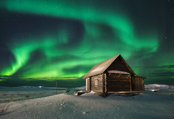 Landscape with northern lights over a wooden house on the coast of the Barents Sea on the Kola...