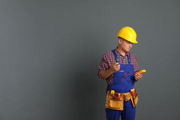 Electrician with multimeter wearing uniform on gray background. Space for text - Powered by Adobe
