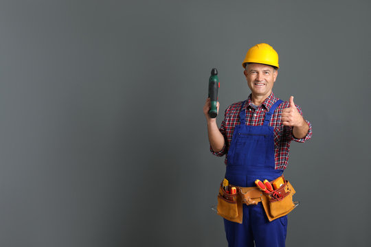 Electrician with drill wearing uniform on gray background. Space for text