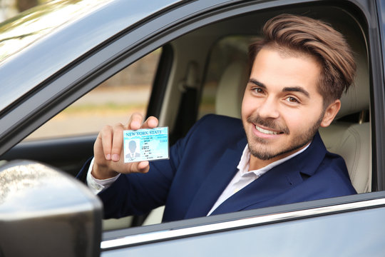 Young man holding driving license in car