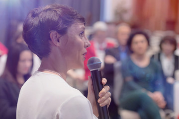 Beautiful business woman with microphone in her hand speaking at the  conference or seminar.