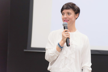 Beautiful business woman with microphone in her hand speaking at the  conference or seminar.