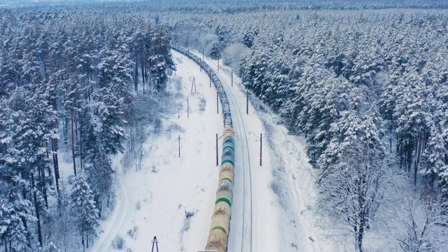 Aerial view of the freight train, carrying tank cars with oil and cargo containers, moving on the winter snowy forest