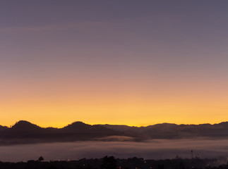 A village surrounded by mountains with foggy morning time and orange sky, beautiful landscape