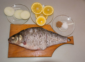 Bream on a wooden cutting board with onions, lemon and spices