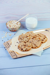 Oatmeal cookies with dried fruits, seeds, cranberries on a wire rack. On wooden gray background with a glass of fresh warm milk and oatmeal