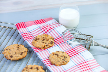 Homemade chocolate cookies on a wire rack, just from the oven, on a wooden gray background, around milk and kitchen towel. Top view