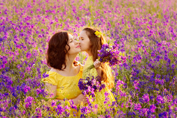 Obraz na płótnie Canvas Portrait of a daughter kissing mother on a beautiful flowering meadow