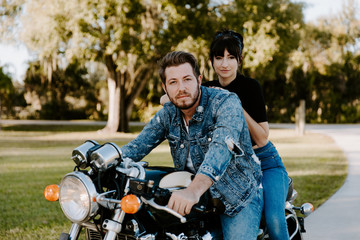 Fototapeta na wymiar Portrait of Attractive Good Looking Young Modern Trendy Fashionable Guy Girl Couple Riding on Green Motorcycle Cruiser Old School Classic Vintage Bike Smiling Casual Cool Relaxed Dating Hugging Love