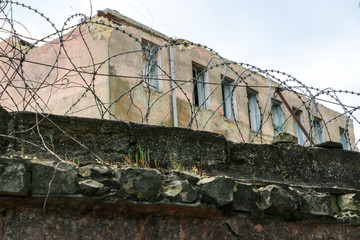 Half-ruined building and a fence with barbed wire. Closed and guarded territory. Abandoned area.