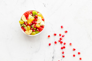 Fruit diet concept. Fruit salad with apple, kiwi and pomegranate in bowl on white stone background top view copy space