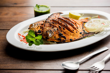 Tandoori Pomfret fish cooked in a clay oven and garnished with lemon , mint, cabbage and carrot salad. Selective focus