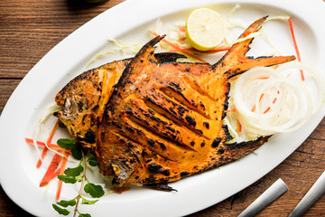 Tandoori Pomfret fish cooked in a clay oven and garnished with lemon , mint, cabbage and carrot salad. Selective focus