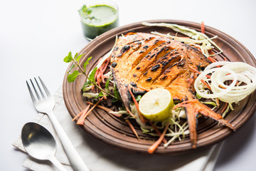 Tandoori Pomfret fish cooked in a clay oven and garnished with lemon , mint, cabbage and carrot salad. Selective focus