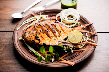 Tandoori Pomfret fish cooked in a clay oven and garnished with lemon , mint, cabbage and carrot salad. Selective focus