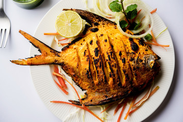 Tandoori Pomfret fish cooked in a clay oven and garnished with lemon , mint, cabbage and carrot salad. Selective focus
