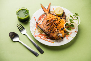 Tandoori Pomfret fish cooked in a clay oven and garnished with lemon , mint, cabbage and carrot salad. Selective focus